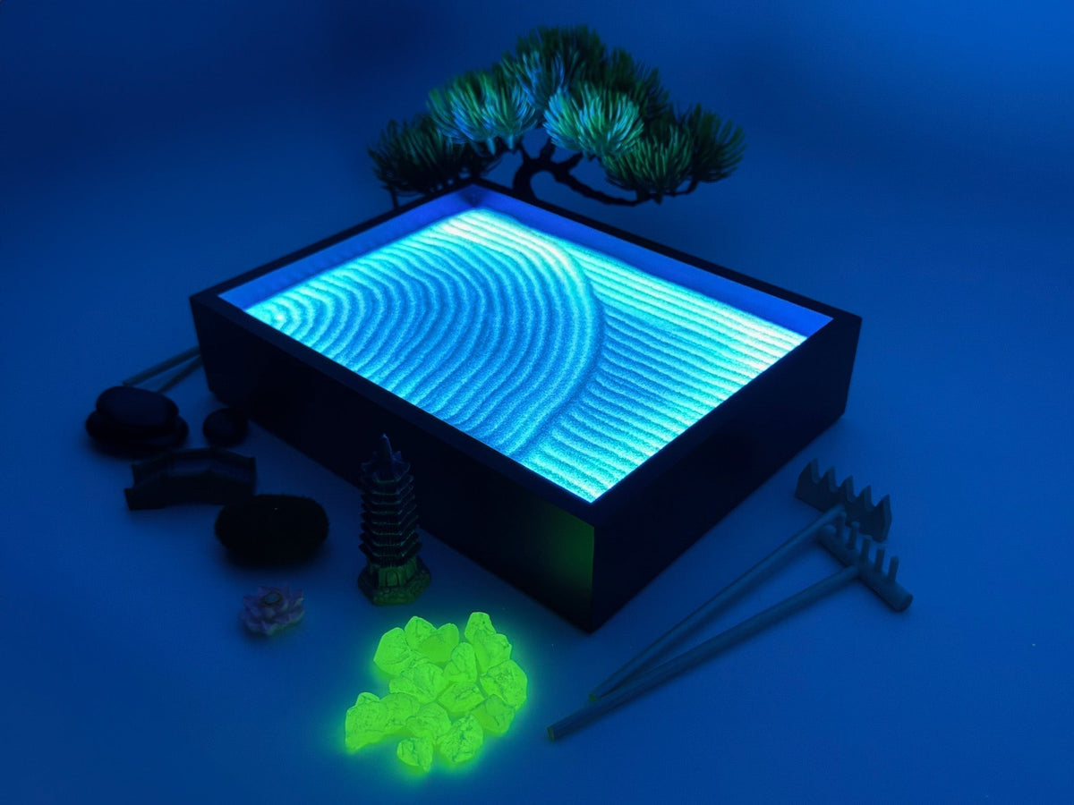 Aura Zen Garden glowing blue under UV light with a bonsai tree, rakes, and green glow stones